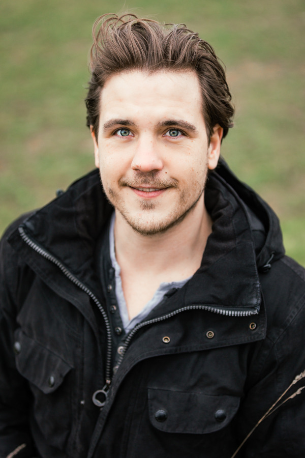 Freundliches Foto von Maximilian Sordon vor einem dunklen Hintergrund